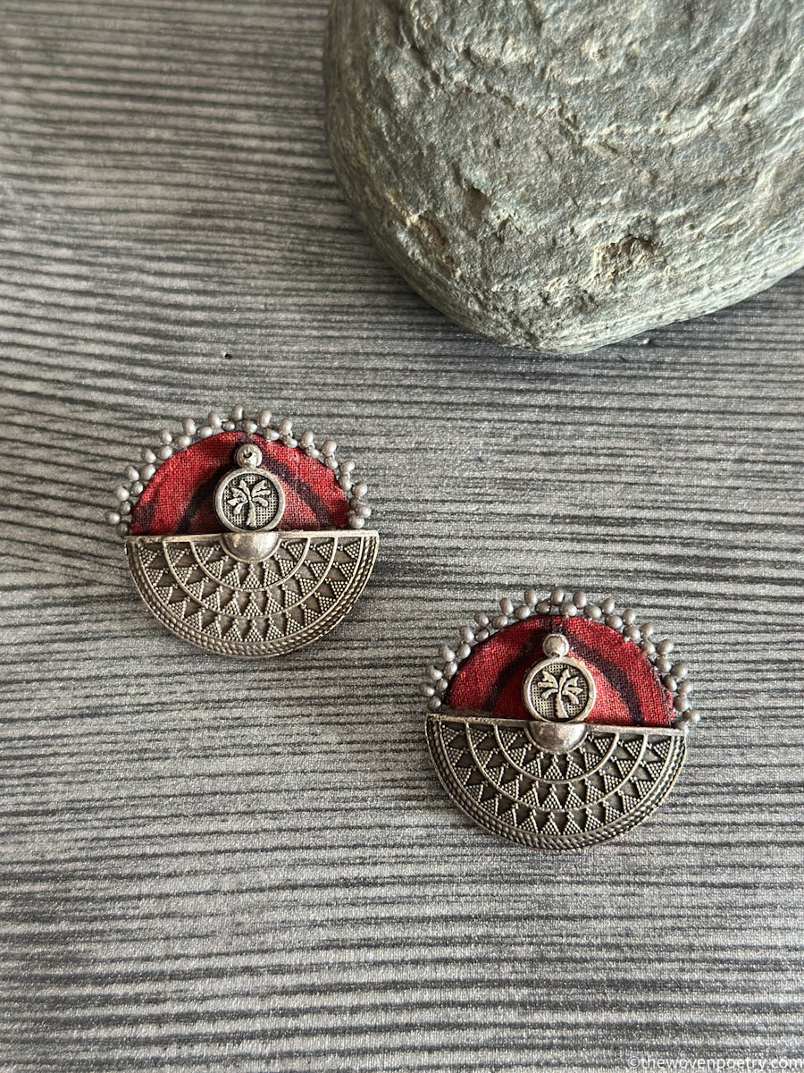 Pair of silver earrings with red fabric on a textured surface
